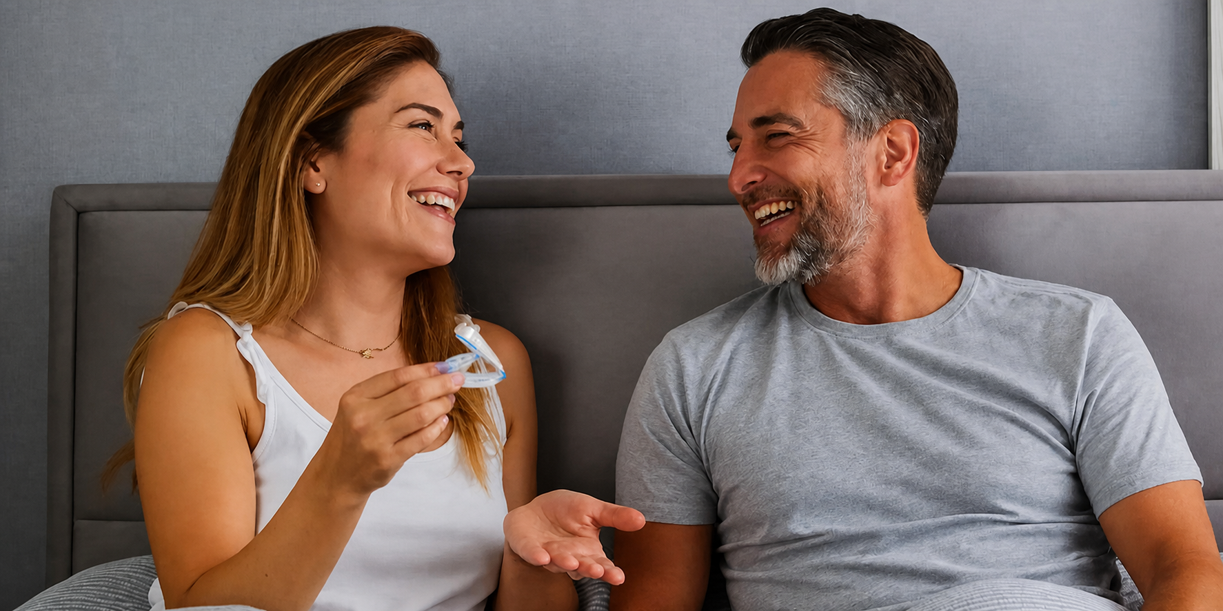 Smiling couple sitting in bed while holding a QuietLab anti-snoring mouthpiece